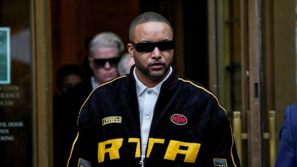 Stylist Deonte Nash, wearing a black and yellow jacket, blue shirt underneath and sunglasses, exits the courthouse.