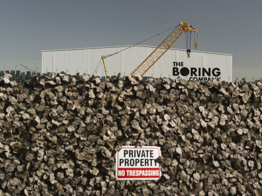 A view of the Boring Company building with a wall in the foreground, including a sign that says "private property no trespassing"