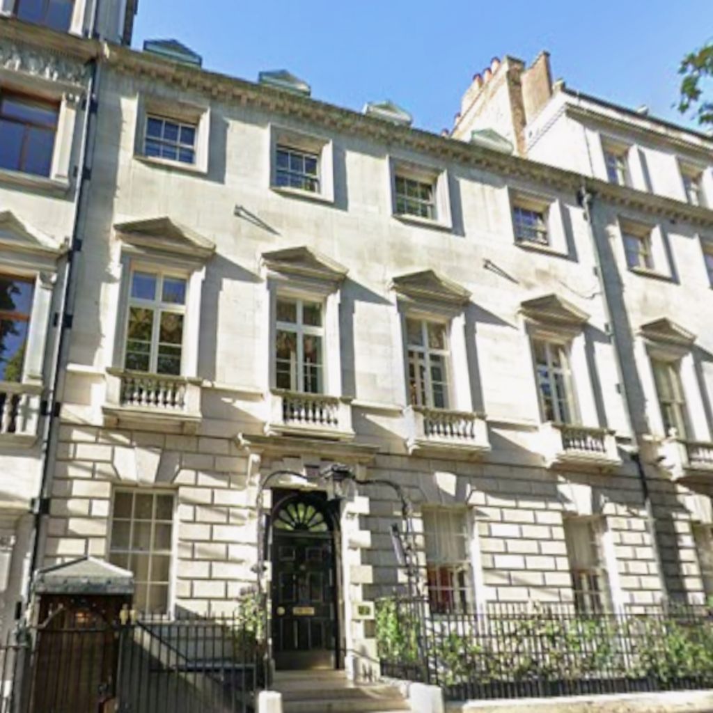 The exterior of Annabel’s private members’ club in central London, showing a pale stone Georgian-style townhouse with tall sash windows, decorative pediments, a black arched doorway and railings along the pavement in bright daylight.