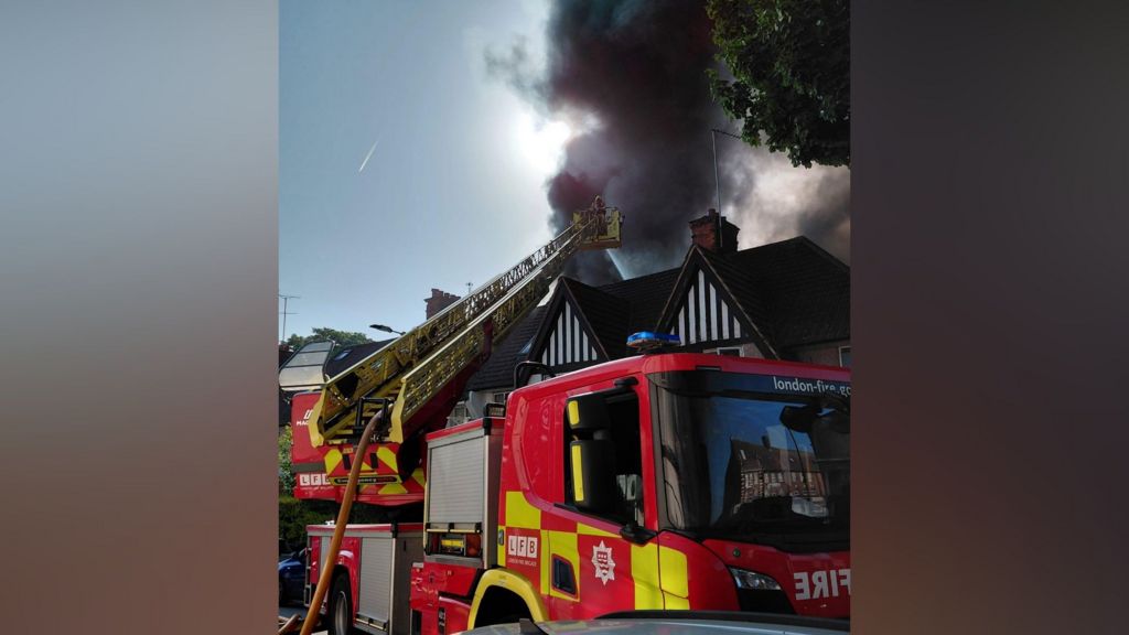 Red fire engine with yellow ladder and black plumes of smoke