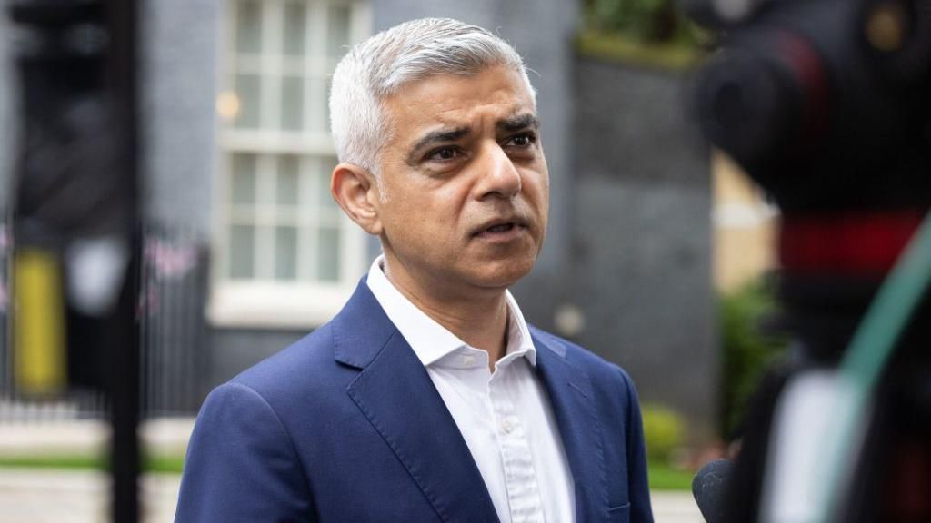 Sadiq Khan standing in a street, wearing a blue jacket and white shirt