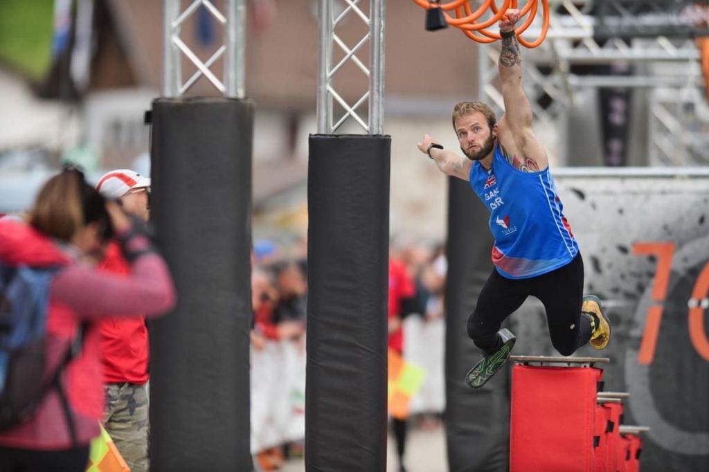 Adaptive athlete, Jamie Gane is swinging from rings as part of an obstacle course race. 