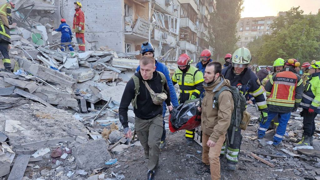 Rescuers at the site of damanged residential buildings with rubble in the background on a sunny day in Kyiv