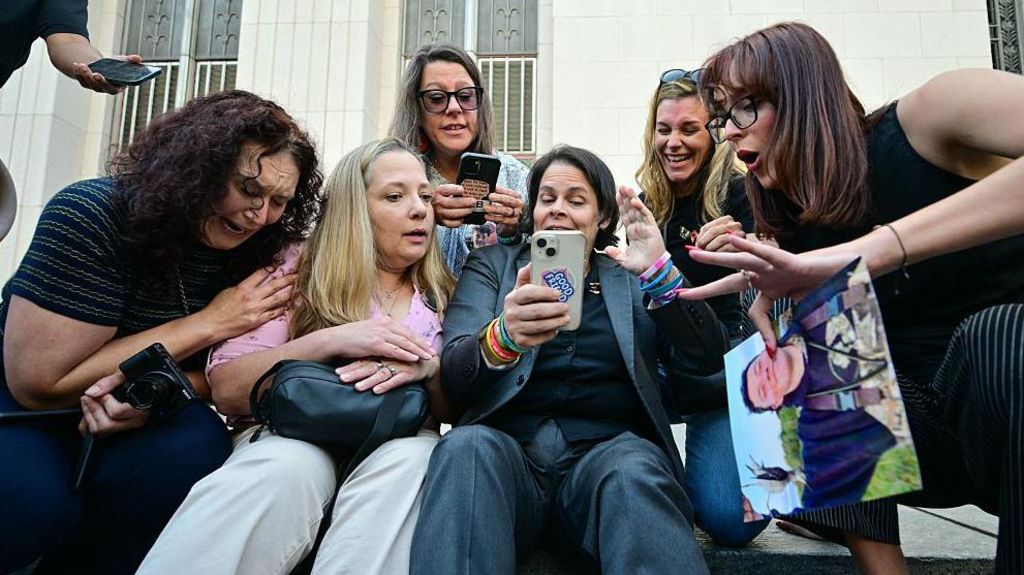 A group of women sit on steps in front of an Los Angeles courthouse and react with happiness and tears at verdict 