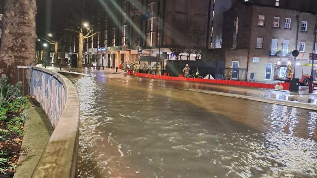 Road with water flowing down it. A tree is on the left. It is night time.