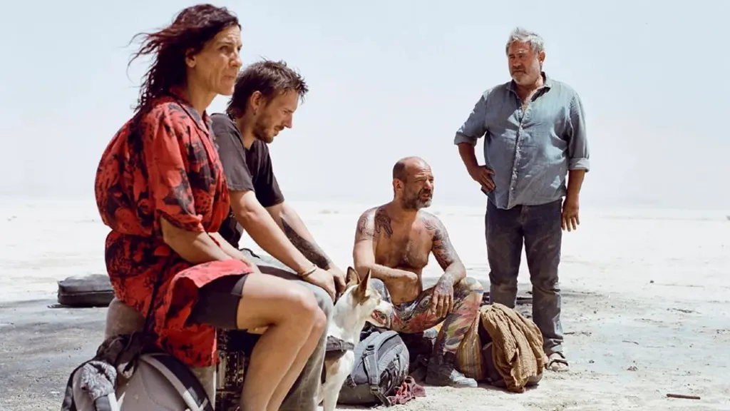 A promotional still image from the film Sirat showing four people sitting in the desert