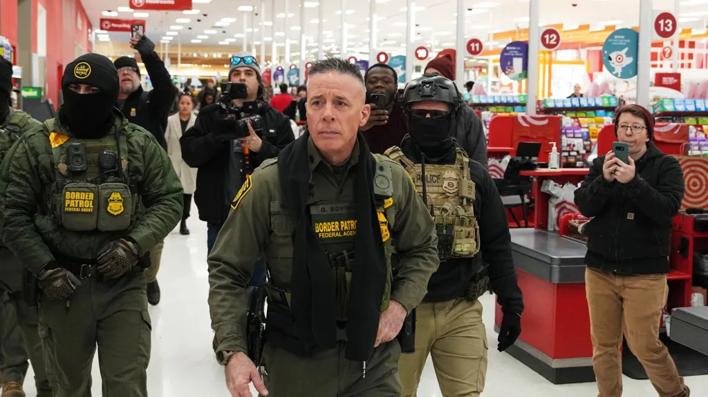Bovino is in the centre wearing Border Patrol uniform, flanked by several others either side, as they walk alongside cashiers in a Target store