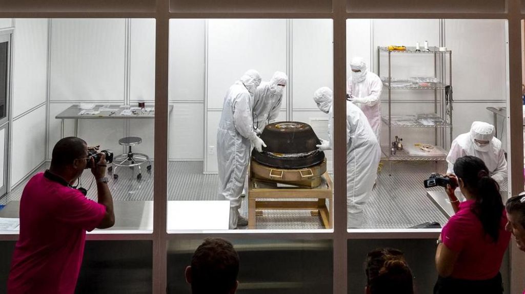 A Nasa team dressed in white suits and masks examining a space capsule in a cleanroom.