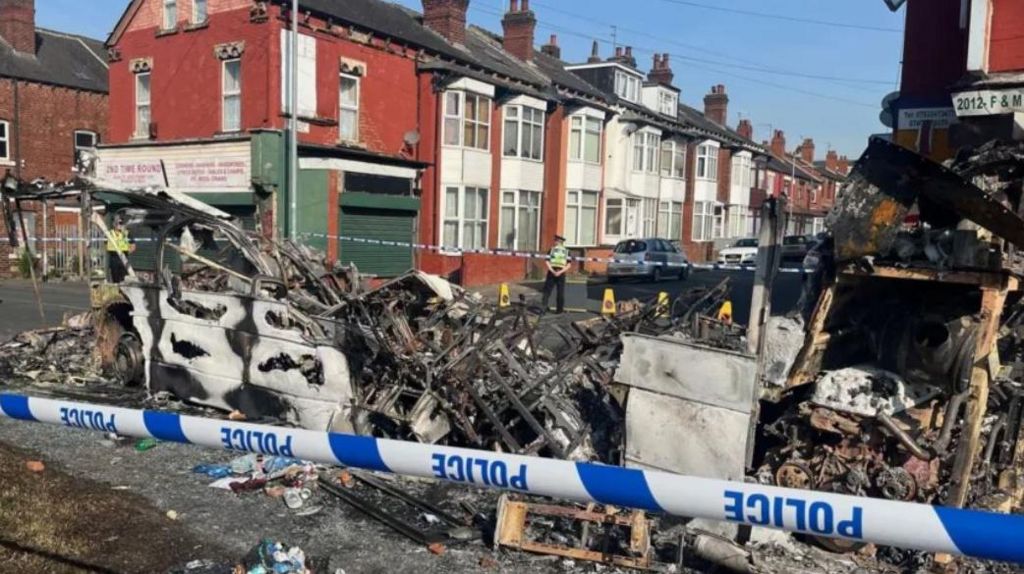 Police tape around the charred remains of a vehicle in a Harehills street