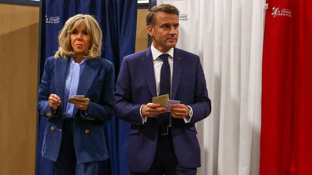 France's President Emmanuel Macron (R) and his wife Brigitte Macron (L) exit a polling booth, adorned with curtains displaying the colors of the flag of France, before casting their ballot for the European Parliament election at a polling station in Le Touquet, northern France on June 9, 2024