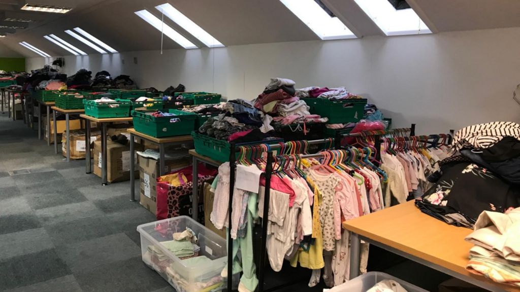 A clothes rail with children's clothes and boxes at HQ of Ruksak 45218 in Trowbridge of folded clothes in the background
