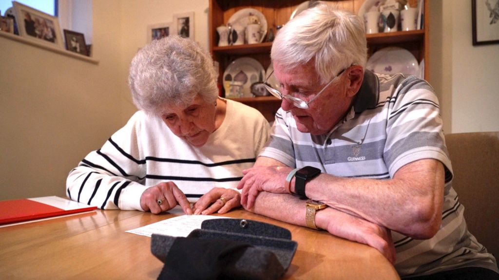 Maureen and Eric, both 85, are looking over the invoice they were given. They are sitting at a table together reading the invoice