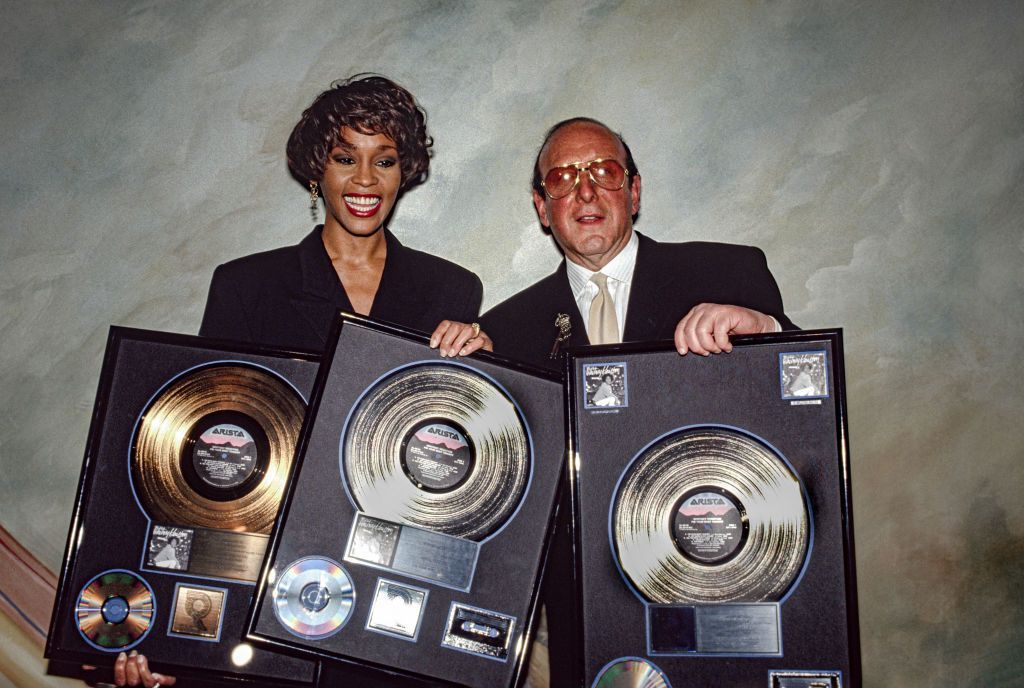Whitney Houston and Clive Davis hold up a collection of gold and platinum records, celebrating the success of her album I'm Your Baby Tonight