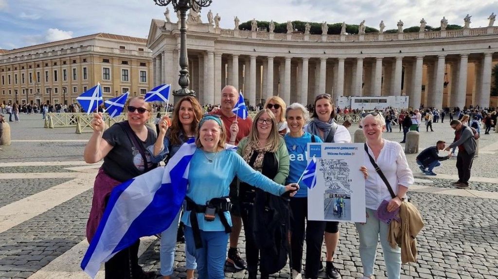 A group of people stand with Scottish flags and banners.
