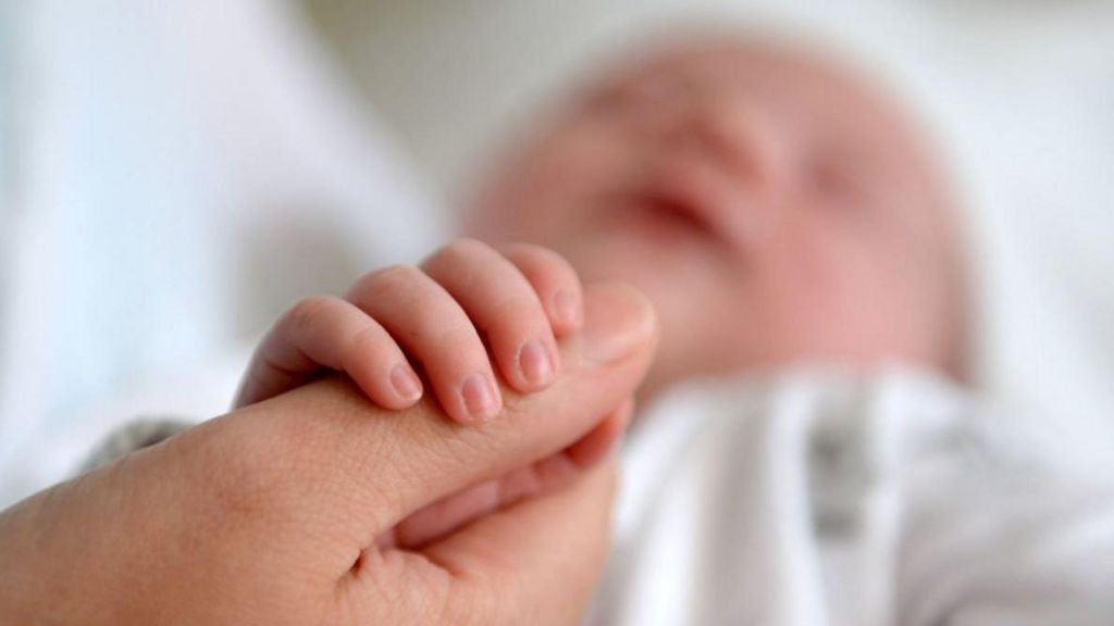 File image showing an anonymous out-of-focus baby grabbing an adult's thumb