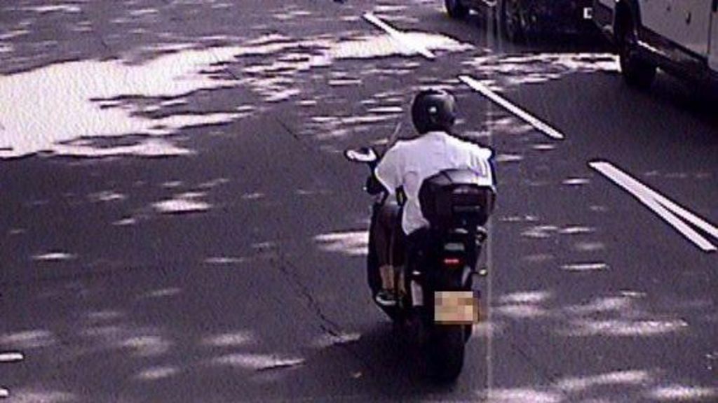 A moped with a rider in a white shirt wearing a helmet. The marking on the road can be seen to the right of him. 