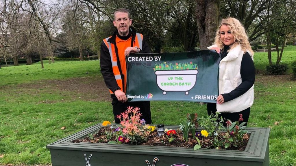 Dave Poulton and his daughter holding a banner, standing beside one of the planters 