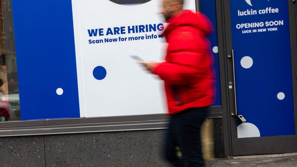 A 'now hiring' sign is displayed in a business's window in Manhattan on January 09, 2026, in New York City. 