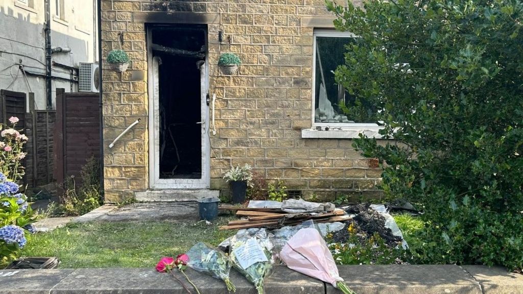 Three bunches of flower left on a wall outside a house damaged by fire 