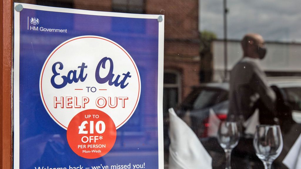 An Eat Out to Help Out poster in a window with two wine glasses and a blurred reflection of a customer