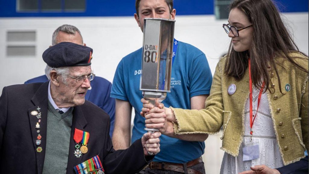 British WWII veteran Jim Grant (L) holds the 'Torch of Commemoration' with a French member of the Commonwealth War Graves Commission at their arrival at Caen-Ouistreham ferry terminal