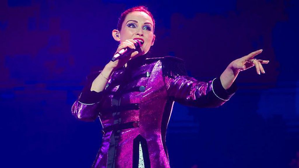 Sophie Ellis-Bextor is performing in stage wearing a reflective purple coat.