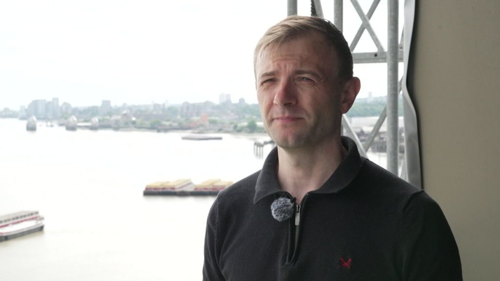 Craig Robinson stands on his balcony. Scaffolding can be seen behind him
