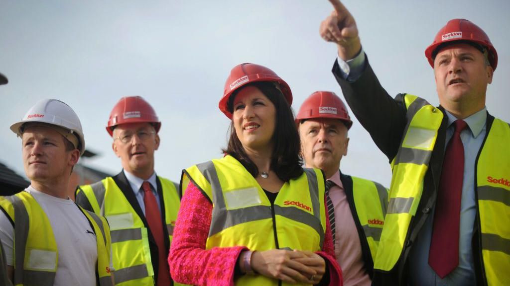 Rachel Reeves and Ed Balls, pictured in 2012 visiting a social housing project with other Labour frontbench colleagues, wearing yellow high-vis jackets and red hard hats