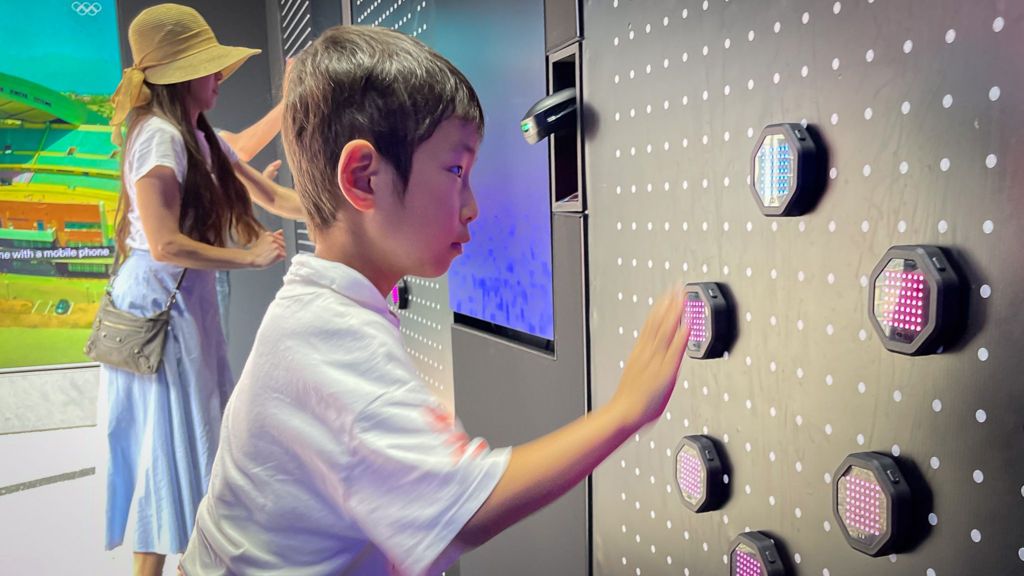 A young boy plays a game where he has to touch illuminated sensors in front of him