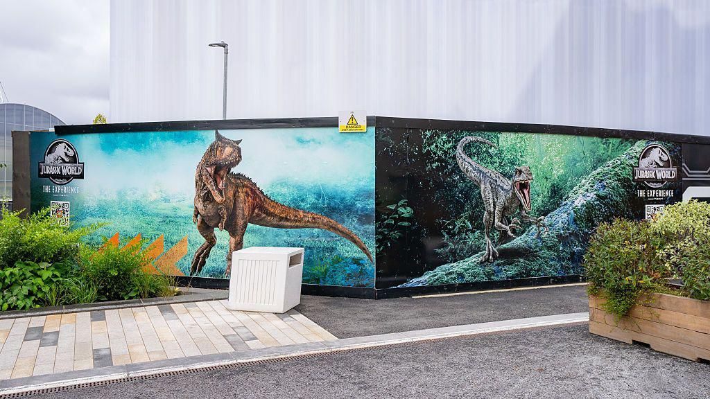 The exterior of the exhibition – there are billboards advertising the Jurassic World experience with pictures of dinosaurs.