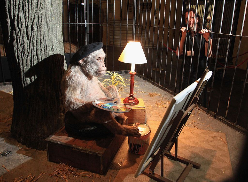 An installation of a monkey with a black beret painting from an easel  