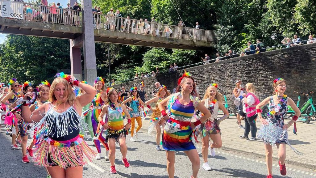 People in rainbow shirts dancing while walking down the street