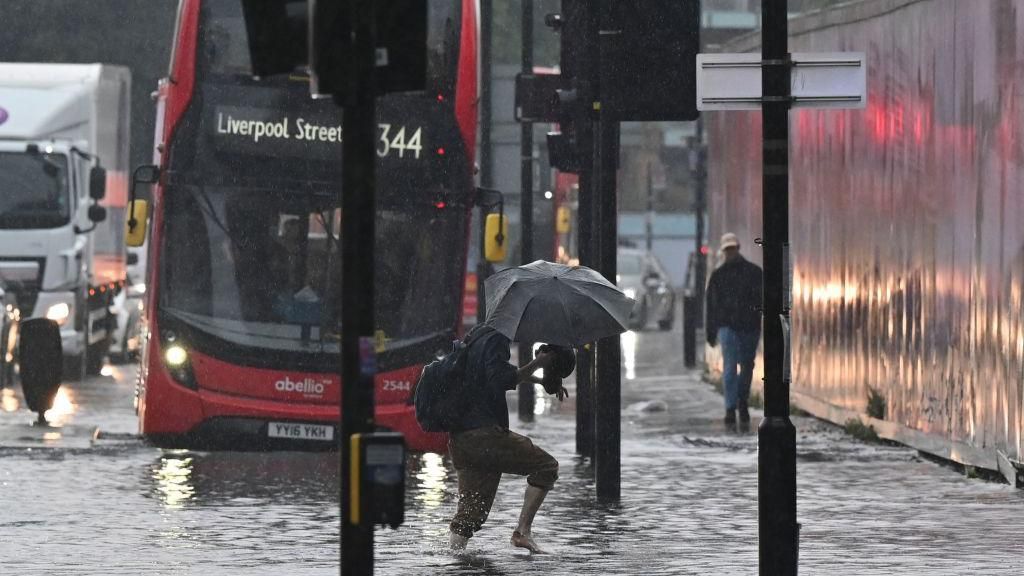 man walking through floods with bus in background