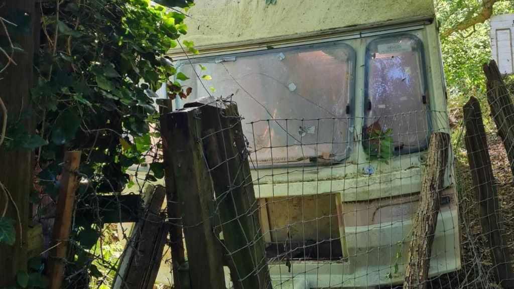 Old caravan next to fence in wooded area