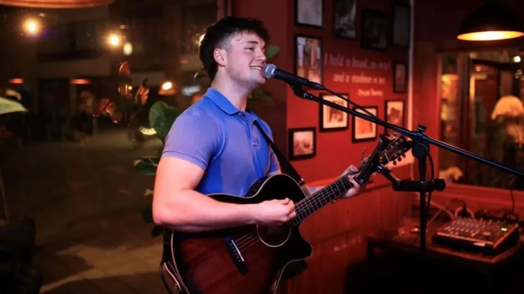 A man in a blue shirt smiling and playing guitar