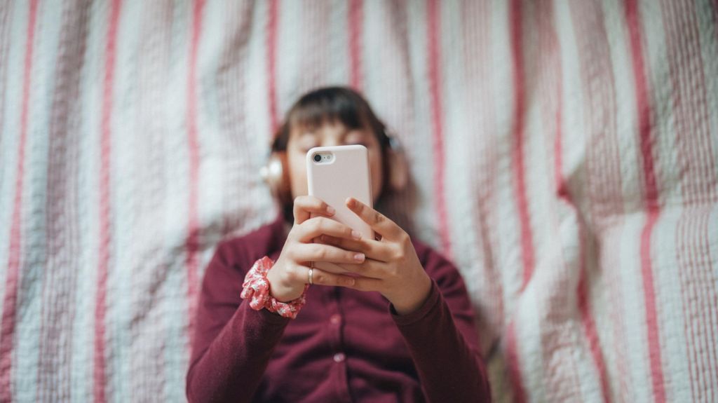 Girl in bed with earphones on looking at her phone
