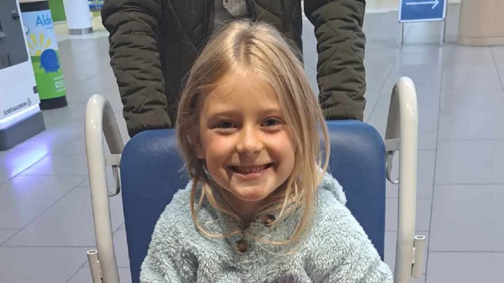 Nansi Alys sits smiling in a wheelchair in a hospital 