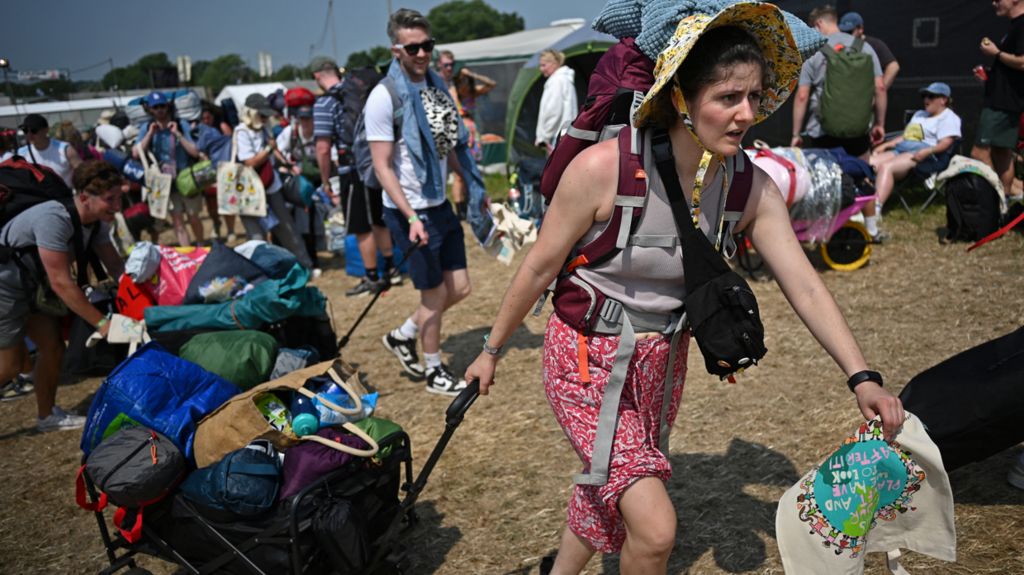 A woman in a yellow sun hat pulling bags in a trolley across festival site