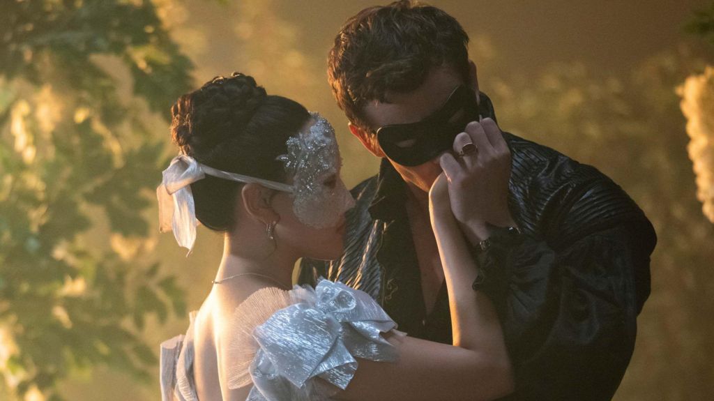 Sophie (Yerin Ha), wearing a silver mask and silver dress, and Benedict (Luke Thompson), wearing a black mask and black bolero jacket.