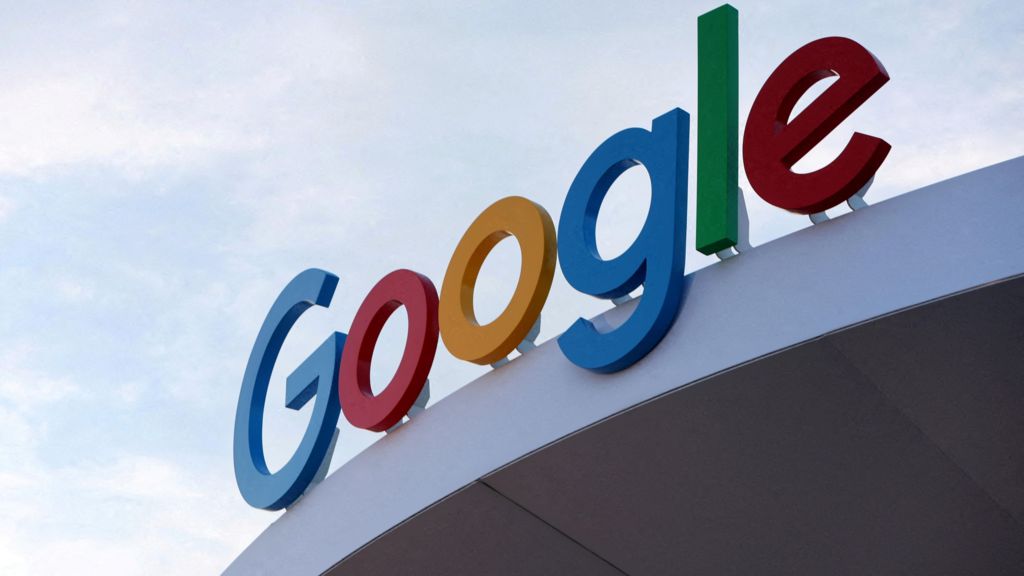 A close-up of Google's logo displayed on a Google building against the backdrop of a blue sky.