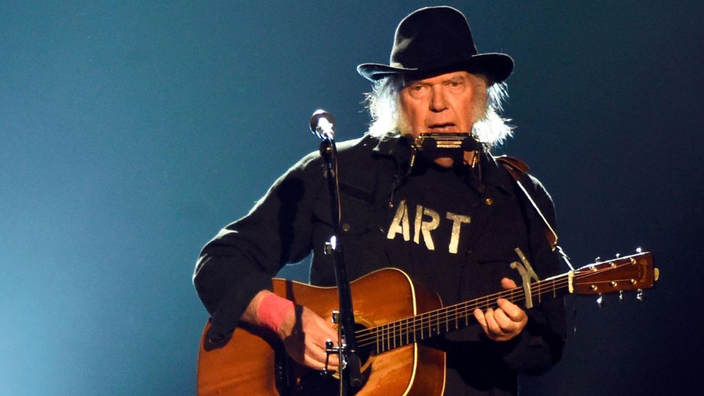 Neil Young plays the guitar and the harmonica, while wearing a black t-shirt emblazoned with the word "art" in gold stencilling.