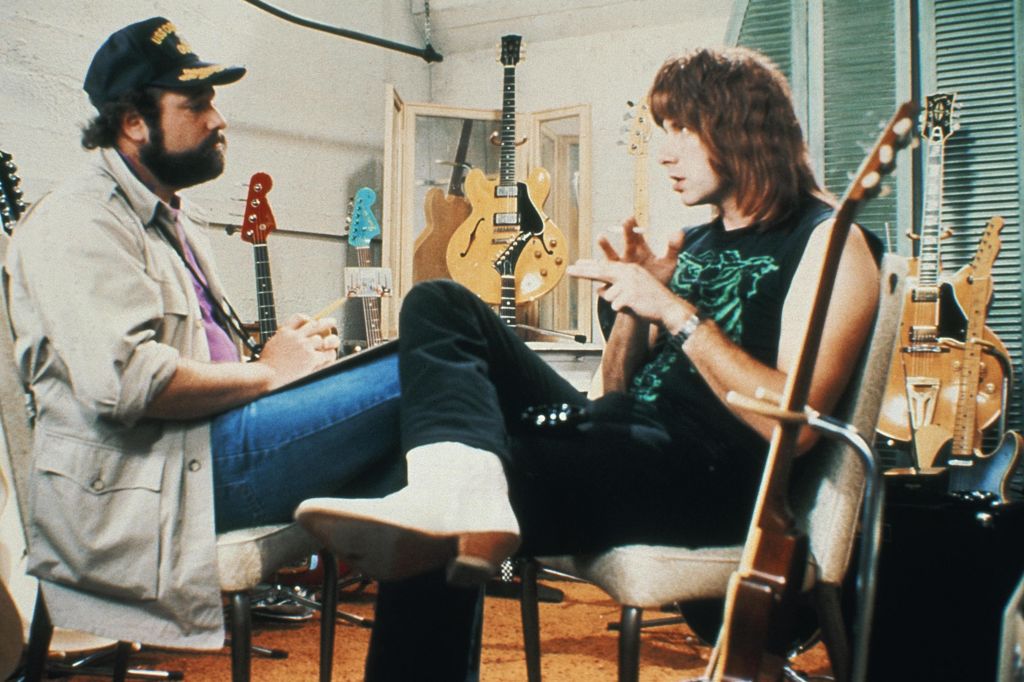 Rob Reiner as on-screen director Marty DiBergi interviewing Christopher Guest as Nigel Tufnel surrounded by guitars in a scene from This Is Spinal Tap
