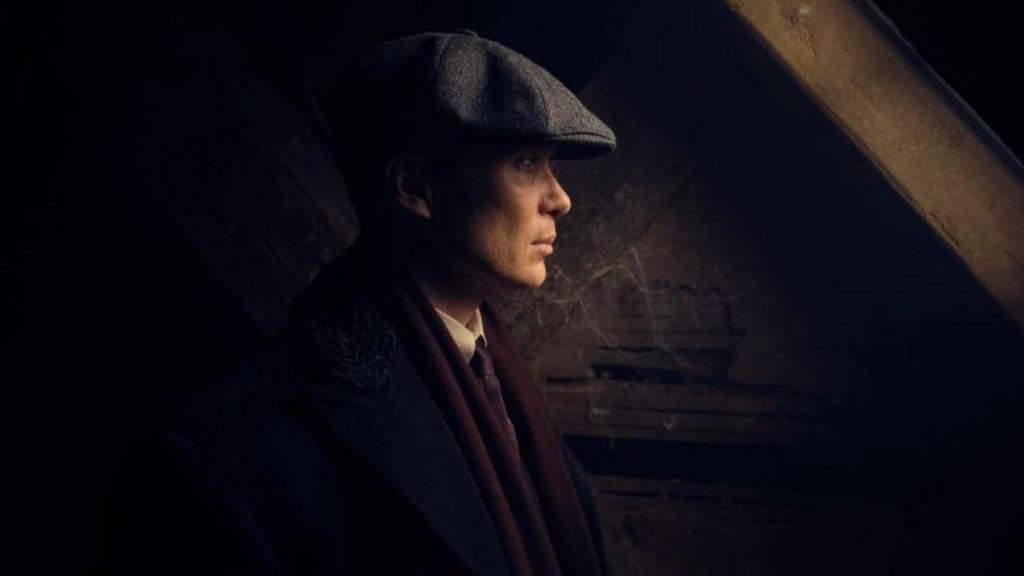 Publicity shot of Peaky Blinders character Tom Shelby, played by Cillian Murphy, wearing a suit, dark red scarf and grey flat cap