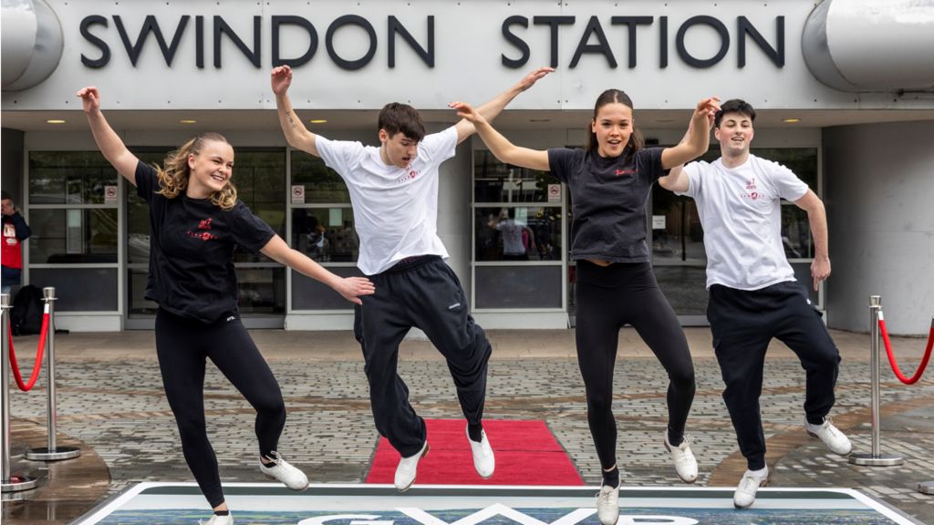 Four tap dancers pictured mid-jump outside Swindon Station. 