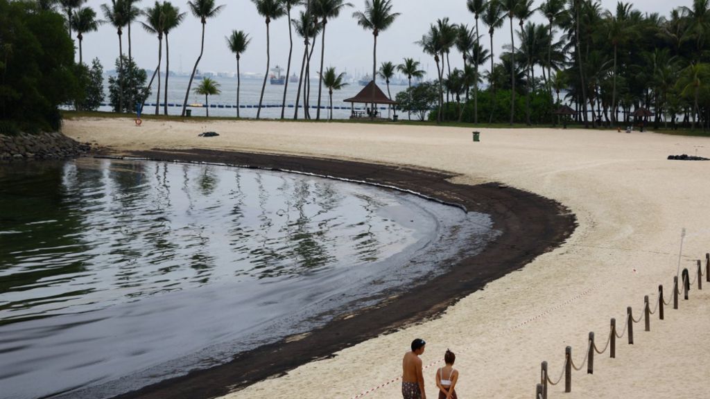 Beach-goers walk next to the polluted oil slick at Tanjong Beach