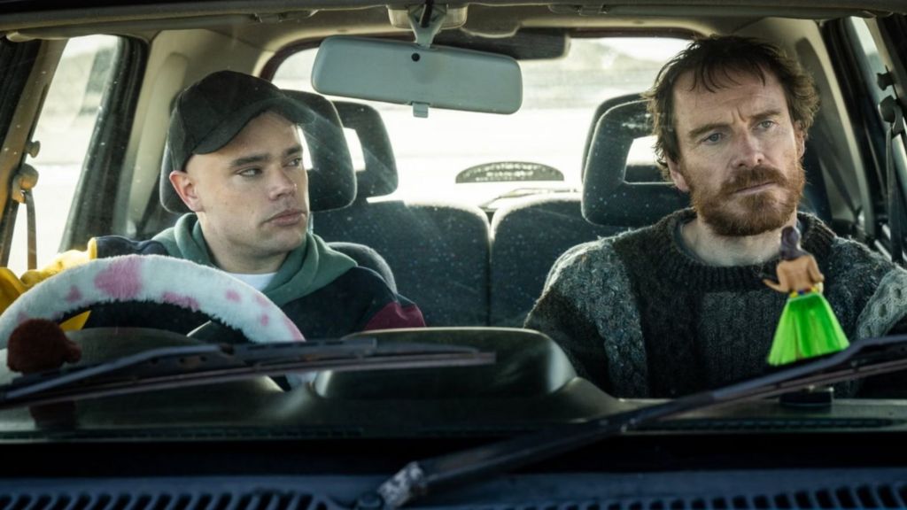 Michael Fassbender and Moglai Bap are pictured in a car, in a scene from the 2024 Kneecap biopic