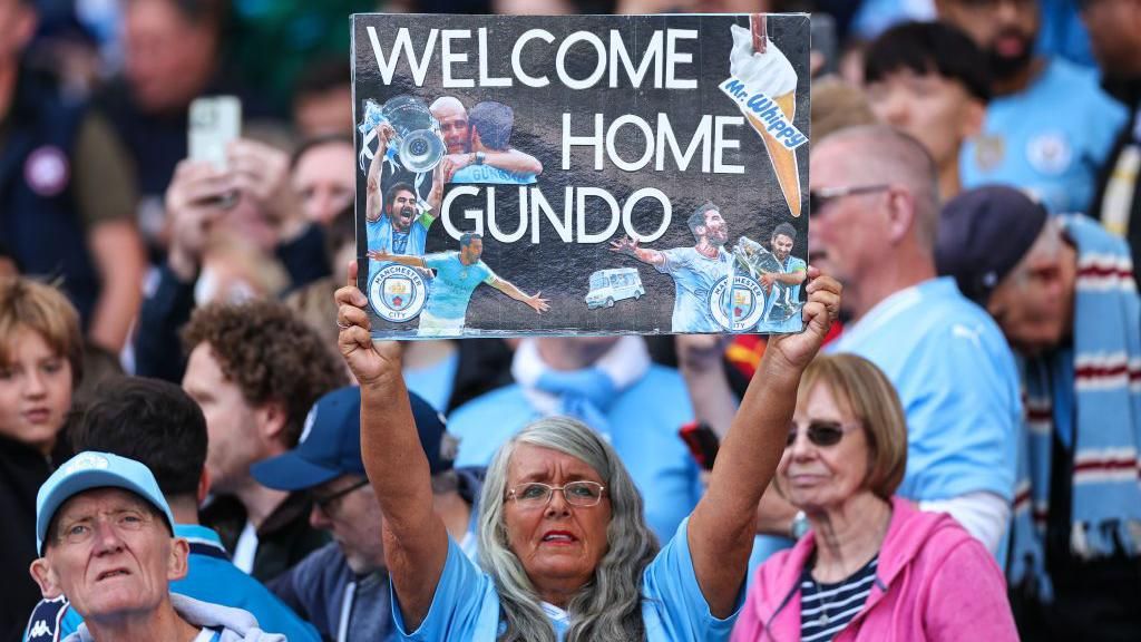 A fan holds up a display card saying "Welcome Home Gundo"