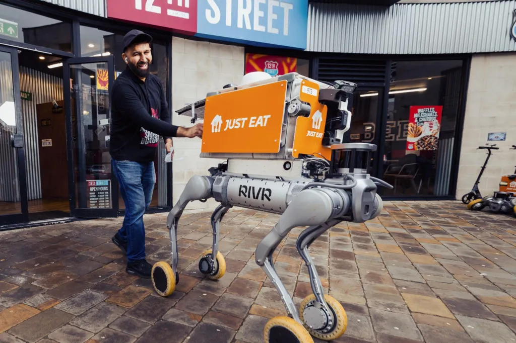 A four‑legged delivery robot on wheels, with an orange Just Eat box on its 