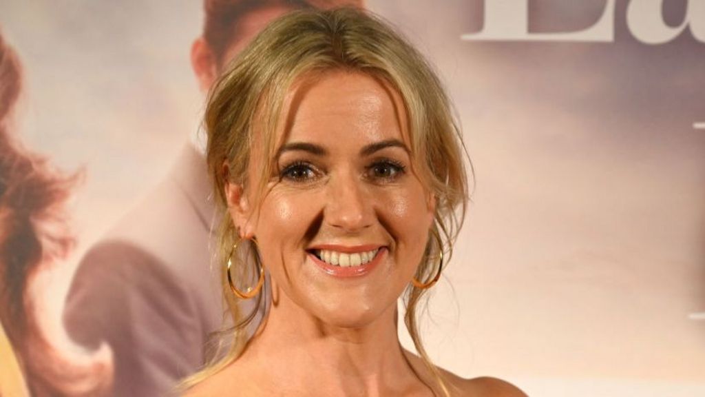 Jojo Moyes pictured smiling on the red carpet. Her blonde her has been tied up into an up-do. 