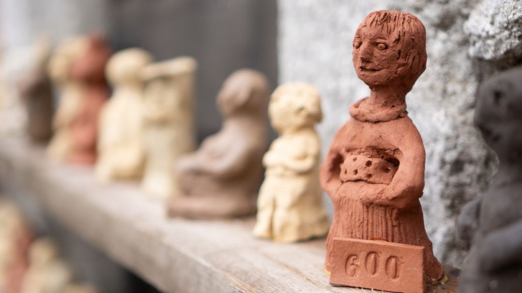 A close-up of a female clay figure on a shelf with other figures in the background